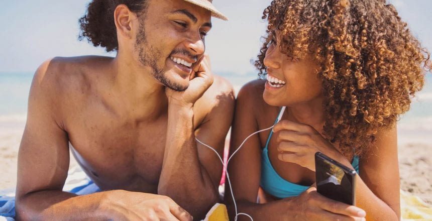 couple-on-beach-listening-to-music-and-smiling-optimized